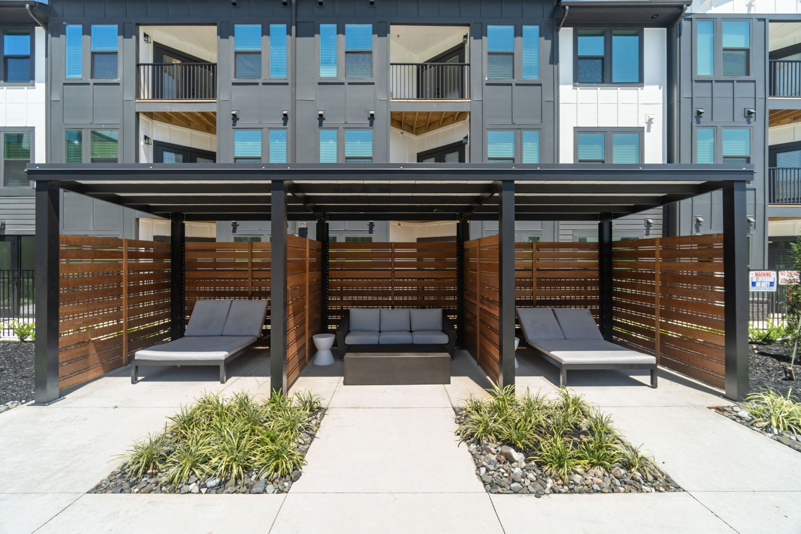 Private poolside cabanas at Evolve at Lake Norman featuring comfortable lounge seating and wooden privacy screens set against a backdrop of the apartment exterior.